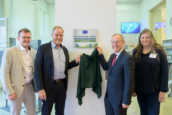 Patrick Child, stellvertretender Generaldirektor der Generaldirektion Umwelt bei der Europäischen Union (EU) (2.v.r.) enthüllt gemeinsam mit Oberbürgermeister Eckart Würzner (2.v.l.), Klimabürgermeister Raoul Schmidt-Lamontain und Umweltamtsleiterin Sabine Lachenicht das EU-Mission-Label „Klimaneutrale und intelligente Stadt“ im Heidelberger Rathaus. (Foto: Philipp Rothe)