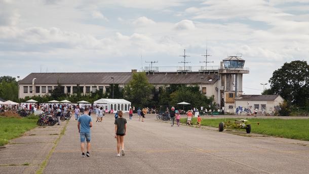 Das Airfield ist im Wesentlichen mit Flughafengebäuden wie dem Tower bebaut. Die Frage, wie die Fläche künftig genutzt werden soll, konnten Bürgerinnen und Bürger beim „Open Airfield“ diskutieren. Einige Menschen laufen auf dem Airfield