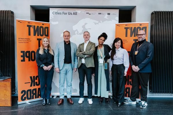 Linda Tinio-Le Douarin, Stellvertretende Leitung der Sektion „Inclusion, Rights and Intercultural Dialogue“ (Inklusion, Rechte und interkultureller Dialog), UNESCO (zweite von rechts) Clare Hart, Vizepräsidentin von Montpellier Méditerranée Métropole & Delegierte für internationale Angelegenheiten und europäische Zusammenarbeit, Stadträtin von Montpellier (Links von Herrn OB) Benedetto Zacchiroli, ECCAR Präsident, Stadt Bologna (rechts von Herrn OB) (Foto: Pohl) Sechs Menschen stehen vor orangefarbenen Roll-Ups.