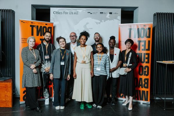 Team der ECCAR Geschäftsstelle beim Amt für Chancengleichheit Dr. Linda Hyökki (von links), Angelo Camufingo, Jana Christ (Danijel Cubelic, Evein Obulor), Nils Vieten, Celina Brook, Marie Paule N’Guessan, (Stefanie Jansen) mit ECCAR Geschäftsführerin Evein Obulor, Danijel Cubelic, Leiter Amt für Chancengleichheit, Stadt Heidelberg und ECCAR Vizepräsident, Bürgermeisterin Stefanie Jansen (Foto: Pohl) Neun Menschen stehen vor orangefarbenen Roll-Ups.