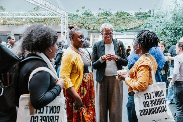 Prof. Dr. Maisha M. Auma, Beirat der Koordinierungsstelle zur nationalen Umsetzung der „UN-Dekade für Menschen afrikanischer Herkunft“ des Bundesamtes für Familie und zivilgesellschaftliche Aufgaben, Deutschland (linke der zwei Frauen in der Mitte) Saraya Gomis, Pädagogin und Mitglied des Expert*innenrats Antirassismus der Bundesregierung (rechte der zwei Frauen in der Mitte) (Foto: Pohl) Menschen unterhalten sich in einem modernen Kongresszentrum.