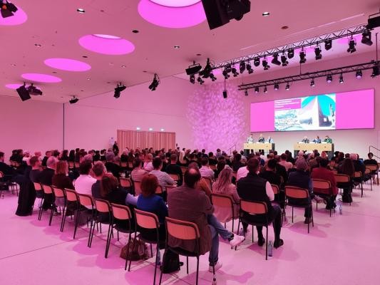 Der Saal im HCC war mit vielen interessierten Branchenvertreterinnen und -vertretern gefüllt. (Foto: Stadt Heidelberg) Stuhlreihen mit Publikum von hinten mit Blick auf die Bühne, auf der ein Podium mit sechs Personen sitzt.