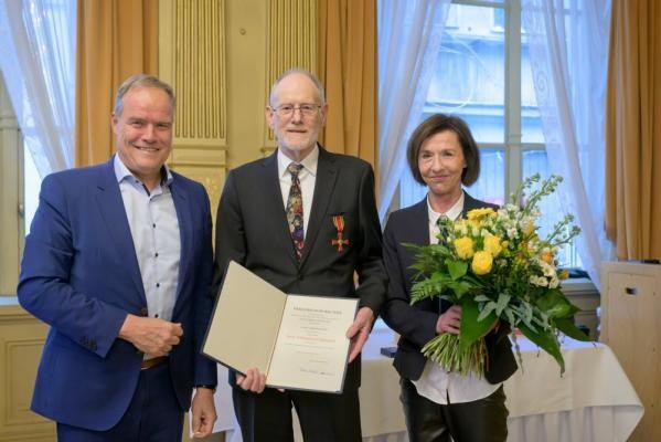 Armin Konrad (Mitte) wurde im Beisein seiner Ehefrau Elke Oeldorf und zahlreicher Gäste für sein herausragendes bürgerschaftliches Engagement und seine Rolle als Initiator, Multiplikator und Brückenbauer zahlreicher Naturschutzprojekte mit dem Bundesverdienstkreuz ausgezeichnet. Oberbürgermeister Eckart Würzner überreichte die Auszeichnung im Spiegelsaal des Prinz Carl. (Foto: Rothe) Oberbürgermeister Eckart Würzner, ein Mann mit Urkunde und eine Fraue mit Blumenstrauß sind zu sehen.