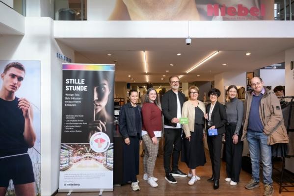 Einkaufen und genießen ohne Reizüberflutung: Das Modehaus Niebel und das Café Nomad bieten in Heidelberg als neues Format die „Stille Stunde“ an (v.l.): Suna Aslan (Café Nomad), Nicolina Visevic (Pro Heidelberg), Bernd und Carmen Niebel (Modehaus Niebel), Bürgermeisterin Stefanie Jansen, Valerie Gebhard (Büro der Kommunalen Behindertenbeauftragten) und Silvan Bock (Youtuber „Autist befragt Prominente“). (Foto: Philipp Rothe) Gruppenfoto der Beteiligten im Modehaus Niebel.