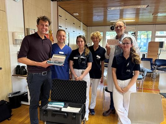 Freuen sich über die neue Kooperation (v.l.): Martijn van der Ent, cue2walk, und die Beschäftigten des SRH Kurpfalzkrankenhauses Timon Wirtz, Brigitte Radzey, Leonie Schmidt, Maria Kabys und Dr. Andreas Becker.(Foto:Cue2walk) 6 Personen in OP-Kleidung und Kittel posiern mit dem neuen Parkison-Gurt.