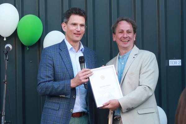 Marc Massoth (links), Leiter des Amtes für Wirtschaftsförderung und Wissenschaft, überreichte Volker Kraft, Geschäftsführer der Bierther GmbH, das Wirtschaftssiegel der Stadt Heidelberg. (Foto: Bierther GmbH) Zwei Herren in Hemd und Jackett halten freudestrahlend eine Urkunde in die Kamera, im Hintergrund einige Luftballons.