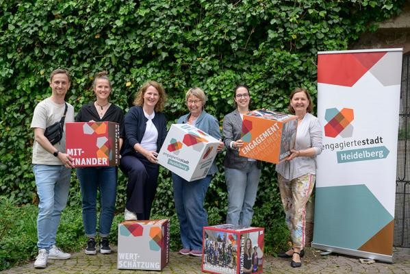 Freuten sich gemeinsam über die Erweiterung des Qualifizierungsnetzwerks für Engagierte in Heidelberg (von links): Jens Ritter (Stadtjugendring), Elisa Itte (Sportkreis), Hanni Derr (Stadt Heidelberg), Beate Ebeling (FreiwilligenAgentur), Jana Fritz (Selbsthilfebüro) und Silke Reck (Volkshochschule). (Foto: Rothe) Sechs Personen posieren mit bunten Kartonwürfeln und einem Aufsteller der Initiative "engagierte Stadt".