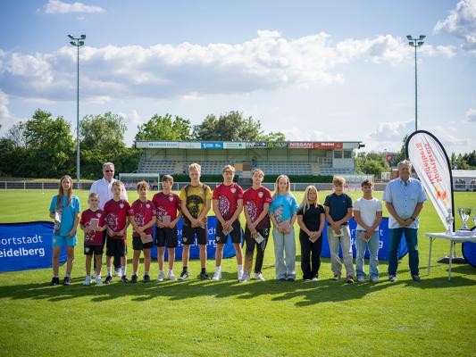 Robert Gleim (7. v. l.) mit seinen Teammitgliedern vom AC Germania Rohrbach wurde Jugendsportler des Jahres. (Foto: Dittmer) Eine Gruppe junger Schüler posiert mit zwei Herren und einer Dame auf einem Sportfeld.