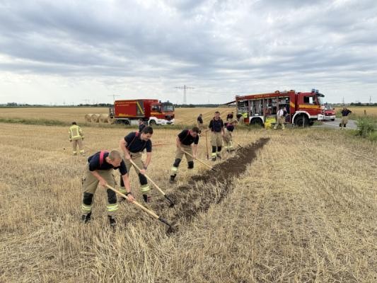 Eine Kette aus Feuerwehrmännern graben den Acker um und legen einen Wundstreifen an