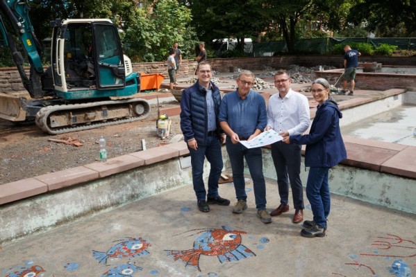 Bürgermeister Raoul Schmidt-Lamontain, Dezernent für Umwelt, Klimaschutz und Mobilität (3. von rechts), besichtigte mit (von links) Andreas Lippke, Fachbereichsleiter Stadtplätze, Grünanlagen und Bäume an Straßen beim Landschafts- und Forstamt, Bauleiter Joachim Becker und Karen Engelhardt, Projektleiterin beim Landschafts- und Forstamt, die Sanierungsarbeiten am Brunnen in der Kurfürsten-Anlage. (Foto: Stadt Heidelberg) Bürgermeister Raoul Schmidt-Lamontain steht mit Andreas Lippke, Joachim Becker und Karen Engelhardt im Brunnenbecken, neben mehreren rot-blauen Fisch-Mosaiken..