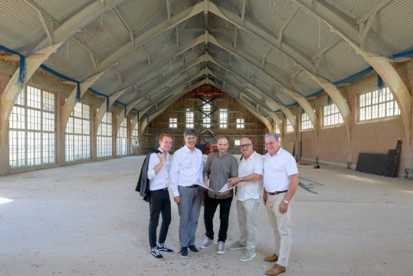 Erster Bürgermeister Jürgen Odszuck (2. v. l.) besucht bei seiner Baustellen-Sommertour die neue Beachhalle auf dem Hospital-Areal gemeinsam mit dem Leiter des städtischen Hochbauamts Marc Tell Feltl, den Architekten Leone Schuch (Hochbauamt) und Stephan Weber (AAg Architekten GmbH) und Gert Bartmann, Leiter des Amts für Sport und Gesundheitsförderung (von rechts). (Foto: Philipp Rothe) Erster Bürgermeister Jürgen Odszuck steht mit Marc Tell, Feltl, Leone Schuch, Stephan Weber und Gerd Bartmann in der neuen Beachhalle. Zu sehen ist die Innenansicht des markanten Daches.