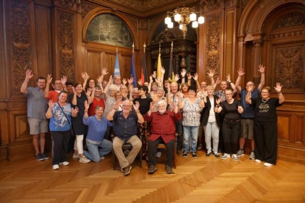 Bürgermeisterin Stefanie Jansen begrüßte Vertreterinnen und Vertreter der Gehörlosenvereine aus Heidelberg und Bautzen am 29. August 2025 im Großen Rathaussaal. (Foto: Stadt Heidelberg) Bürgermeisterin Stefanie Jansen steht mit Vertreterinnen und Vertretern der beiden Gehörlosenvereine im Großen Rathaussaal. Alle heben die Hände nach oben und lächeln.