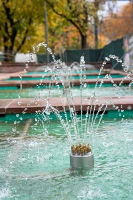 Wasserspiel im Detail: Neue, einstellbare Düsen der sanierten Brunnenanlage an der Kurfürsten-Anlage. (Foto: Christian Buck) Zu sehen ist eine der neuen einstellbaren Düsen der sanierten Brunnenanlage. Sie versprüht Wasser in mehreren Strahlen in einem seichten, türkisfarbenen Becken.