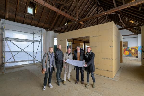 Eine Multifunktionsbox als Haus-in-Haus-Lösung wurde in der Chapel auf dem Hospital-Areal in den Raum gestellt (im Hintergrund). Leone Schuch (Hochbauamt; von links), Moritz Hettich und Stephan Weber (Büro AAg Architekten), Erster Bürgermeister Jürgen Odszuck und Marc Tell Feltl (Leiter Hochbauamt) besichtigten die Baustelle. (Foto: Philipp Rothe) Zu sehen sind 5 nebeneinanderstehenden Personen die einen Plan halten und unter dem Dach der Chapel stehen.