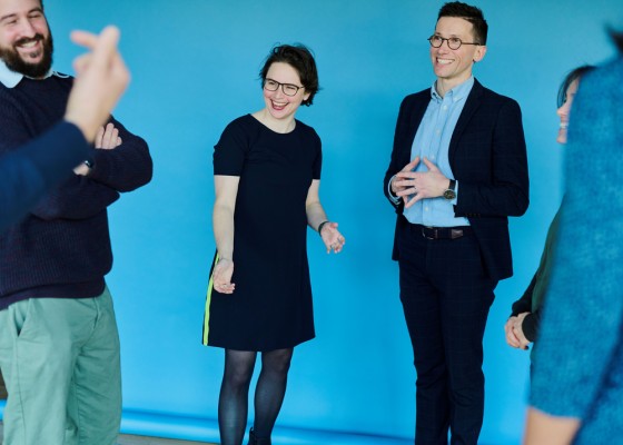 Als Gründerin und Gründer von Mighty Real, einem Beratungsunternehmen für interaktive Veranstal-tungsformate, Team- und Führungskräftetrainings sowie Coachings, unterstützen Elena und Martin R. Lichtenthaler Menschen dabei, schnell in echten Kontakt zu kommen, mutig zusammenzuarbeiten und gelassener mit Komplexität umzugehen. Mehrere Personen lachen.