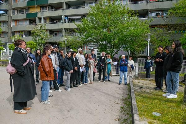 Zahlreiche Teilnehmerinnen und Teilnehmer hörten während des Jane’s Walks den jungen Frauen zu, als sie ihre Gedanken zu Orten im Stadtteil Emmertsgrund teilten, unter ihnen Bürgermeisterin Stefanie Jansen (Mitte). (Foto: Peter Dorn) Ein Foto bei dem links viele Personen, den Personen auf der rechten Seite zuhören,
