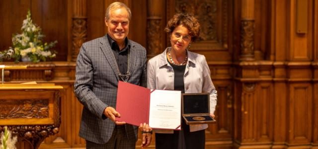 Ein Mann und eine Frau stehen nebeneinander mit der Medaille und einer Urkunde in der Hand