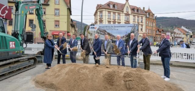 Diverse hohe Vertreterinnen und Vertreter der regionalen Verkehrsverwaltung vollbringen sinnblichlich den ersten Spartenstich auf der Baustelle der Dossenheimer Landstraße, indem sie mit Schaufeln einen Sandberg umgraben