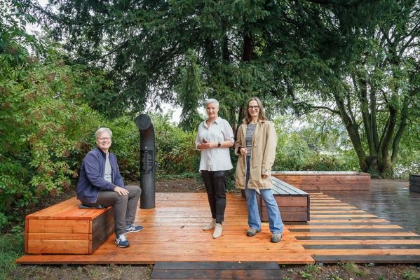 Freuen sich über die neuen Sitzgelegenheiten am Poesiomat: Stefan Kaumkötter (von links) und Dr. Andrea Edel vom Kulturamt der Stadt Heidelberg und Katrin Rulffes vom Verein „NeckarOrte“. Ein Mann und zwei Frauen stehen auf einer neu errichteten Fläche aus Holz mit Sitzbänken und einem periskopartigen Gerät