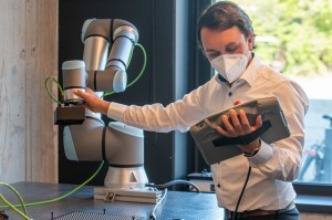 HD Vision Systems ermöglicht es beispielsweise Roboterarmen Gegenstände zu erkennen und zu greifen. (Foto: HD Vision Systems) Ein Mann hält ein Gerät in der Hand, auf der er schaut und berührt einen Roboterarm.