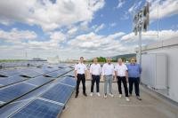 Auf dem Dach von Wohnland Breitwieser befindet sich eine der Sirenen. (Foto: Rothe) Fünf Männer stehen auf einem Dach. Neben ihnen eine Sirene und Photovoltaikanlagen.