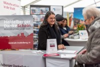 Auch Pro Heidelberg war im Zelt vertreten. (Foto: Dittmer) Eine Frau steht hinter einer Theke und unterhält sich mit jemandem, der davorsteht.
