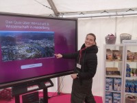 Beim Quiz des Amtes für Wirtschaftsförderung und Wissenschaft ließ sich einiges lernen. (Foto: Stadt Heidelberg) Eine junge Frau steht vor einem Smartboard, auf das sie gleich klicken wird und lacht in die Kamera.