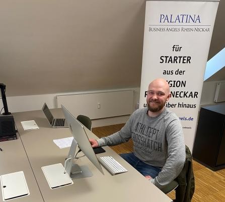 Niklas Duffner in der neuen Geschäftsstelle der Palatina Business Angels auf dem hip. (Foto: Palatina Business Angels) Ein Mann sitzt an einem Schreibtisch und lächelt in die Kamera.