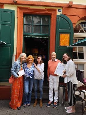 Aline Moser (l.) und Saskia Grössl (r.) von der Stadt Heidelberg gratulieren Jutta Stendel, Christine Hartmann und Dieter Stendel zu 55 Jahren Destille. (Foto: Stadt Heidelberg) Vier Frauen und ein Mann stehen vor einer markanten Haustür. Eine Frau hält eine Urkunde in den Händen.
