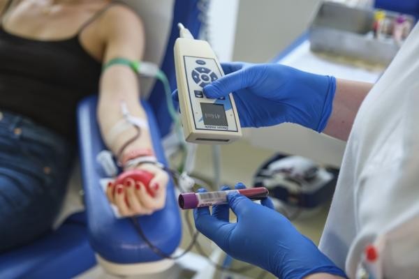 Symbolbild Blutspende. (Foto: DRK-Blutspendedienst Baden-Württemberg - Hessen) Eine Person liegt auf einer Liege und bekommt Blut abgenommen. Eine weitere Person überprüft, dass alles stimmt.