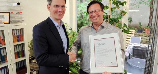 Marc Massoth gratuliert Christian Koinegg zum Firmenjubiläum, schüttelt ihm die Hand, beide lachen in die Kamera.