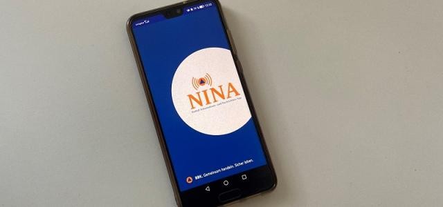 Ein Handy-Display zeigt das Logo der NINA-App.