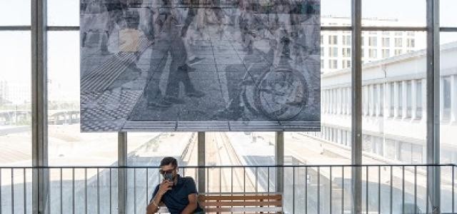 Ein Mann sitzt auf einer Bank unter einer riesigen Fotografie.