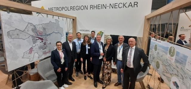 Eine Gruppe aus Männern und Frauen steht an einem Messestand.