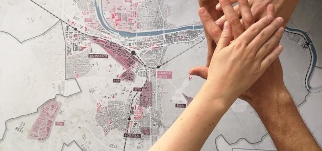 Vier Hände liegen übereinander, im Hintergrund der Stadtplan von Heidelberg.