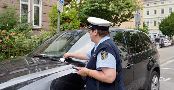 Gemeindevollzugs-Beamter steckt Strafzettel an Windschutzscheibe eines Autos