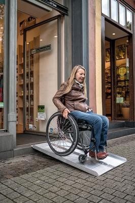 Rollstuhlfahrerin verlässt über mobile Rampe ein Geschäft