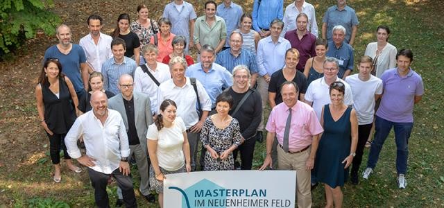 Viele Menschen stehen hinter einem Schild auf dem "Mastplan Im Neuenheimer Feld" steht. (Foto: Universität Heidelberg)