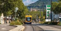 Man sieht eine orangefarbene Straßenbahn in Heidelberg, im Hintergrund ist das Heidelberger Schloss.