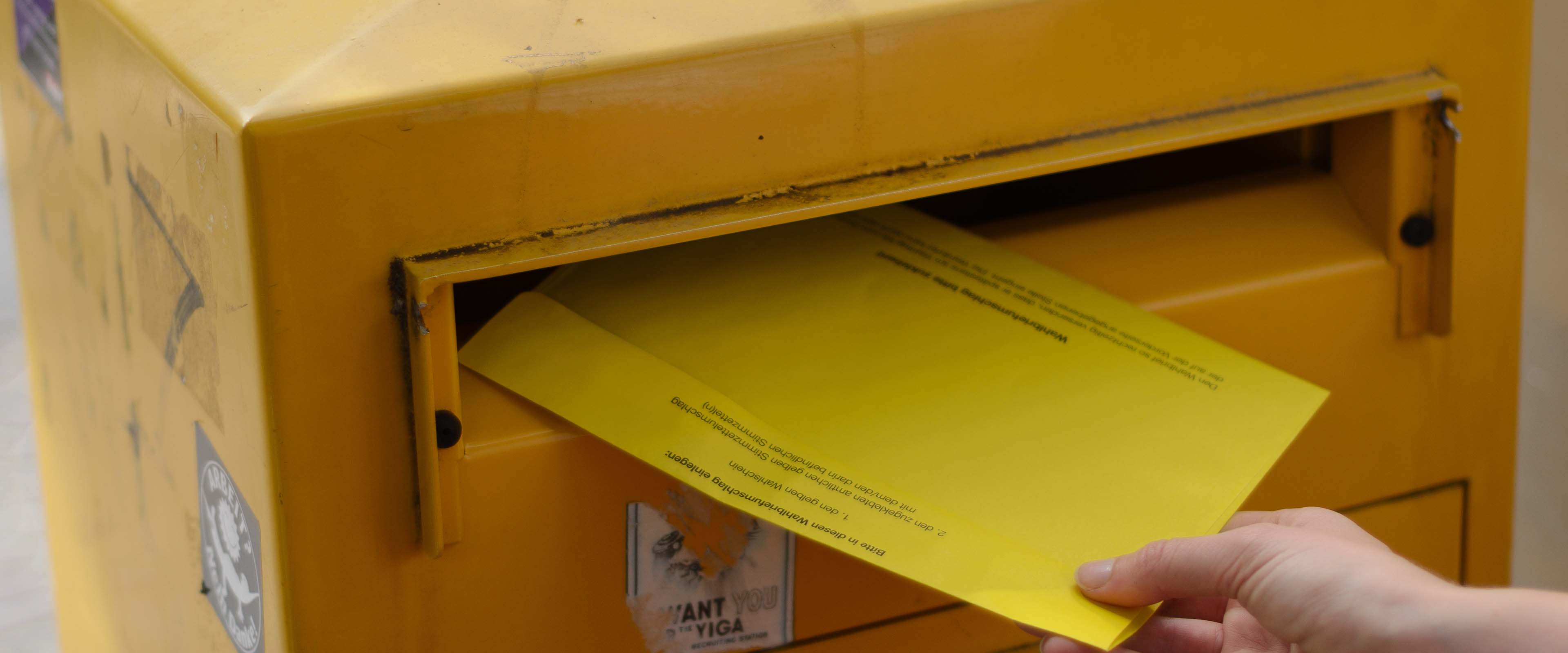 Gelber Briefkasten, in den ein Wahlbrief eingeworfen wird