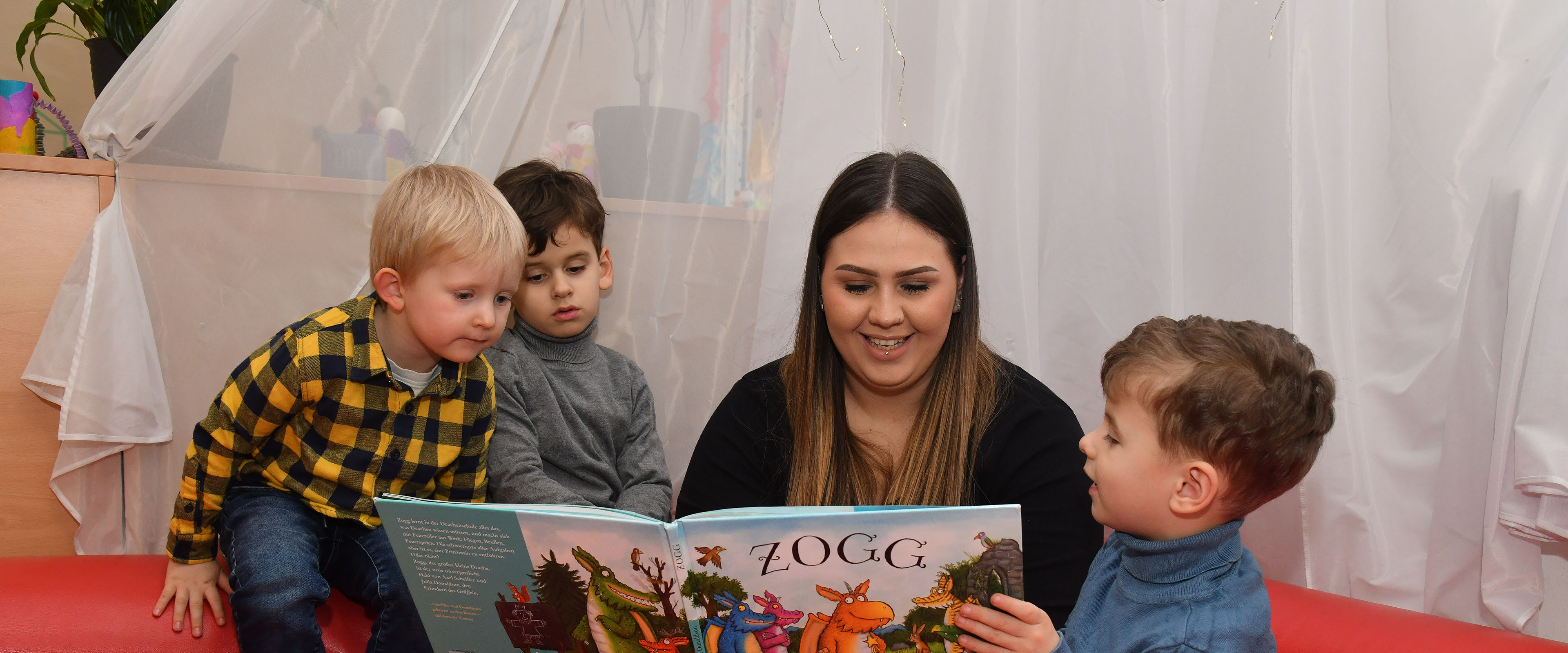 Erzieherin schaut sich mit drei Kindern ein Bilderbuch an
