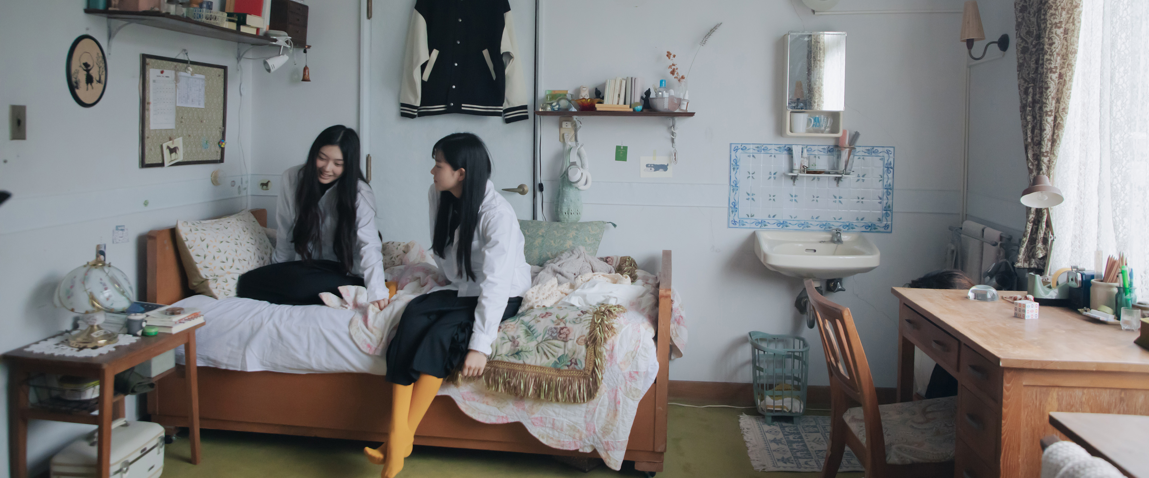 Zwei junge Frauen sitzen in einem Zimmer auf einem Bett und reden miteinander