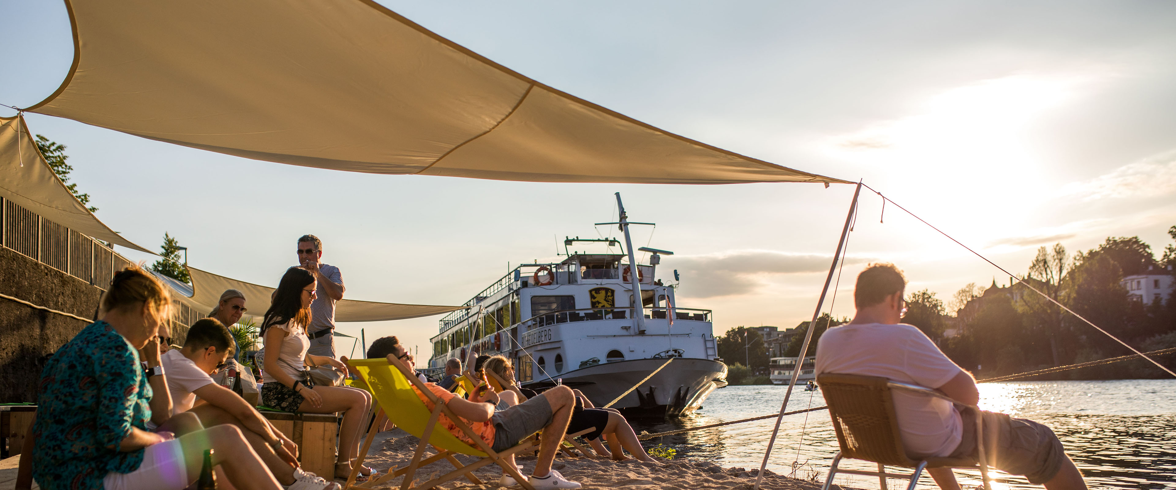 Sandstrand am Neckar mit Sonnensegel, Schiff und Menschen am Ufer