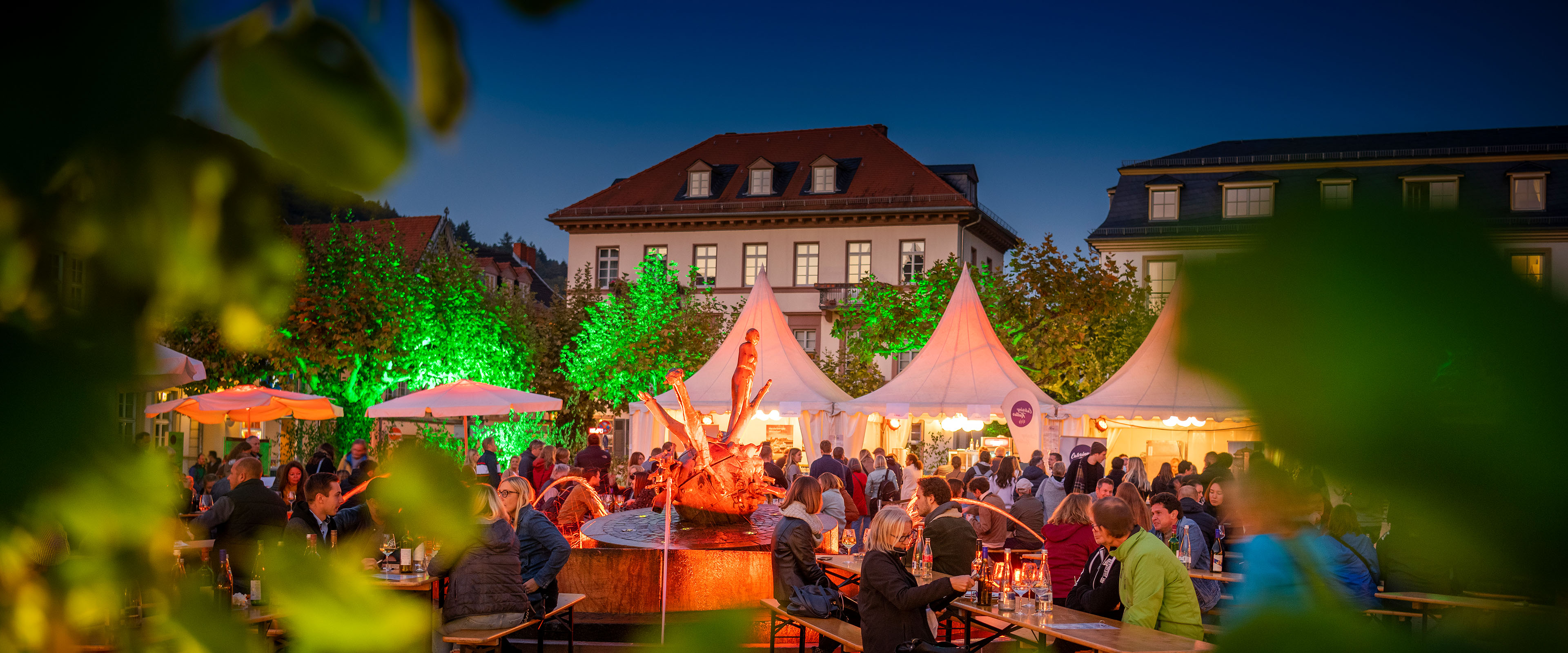 Stimmungsvoll beleuchteter Platz in der Abenddämmerung mit Menschen an Biertischen