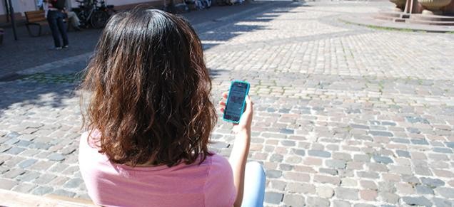 Woman on a bench holding a smartphone (Foto. Stadt Heidelberg)