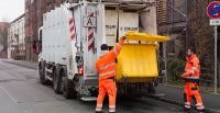 Zwei Männer in orangefarbenem Arbeitsanzug leeren den Inhalt einer Mülltonne in den Behälter des Müllwagens (Foto: Cordes)