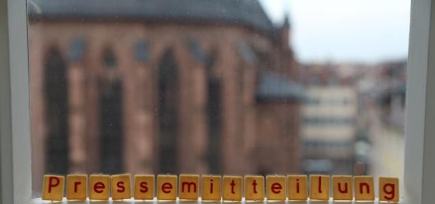 Das Wort "Pressemitteilung" in Scrabble Buchstaben auf eine Fensterbank gelegt. Die Heiliggeistkirche ist im Hintergrund zu sehen.