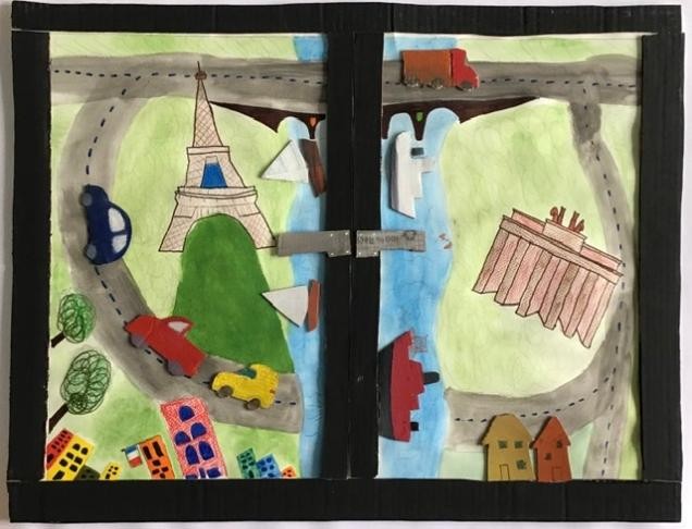 Eine Neuntklässlerin malte und gestaltete einen Fesnterrrahmen mit dem BLick auf einen Fluss in der Mitte, eine Straße mit Autos ringsherum und Sehenswürdigkeiten wie den Eiffelturm und das Brandenburger Tor auf Grünflächen.  
