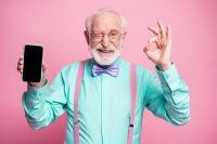 Ein bunt gekleideter älterer Herr mit einem Smartphone in der Hand, der lächelt und zwinkert. 