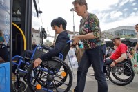 Frau Bürgermeisterin Jansen im Rollstuhl wird von Frau Reiß in einen Bus mit offener Seitentür und ausgeklappter Rampe geschoben.